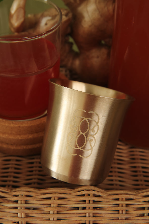 Bronze Ceylai Kansa Cup with logomark on rattan tray.