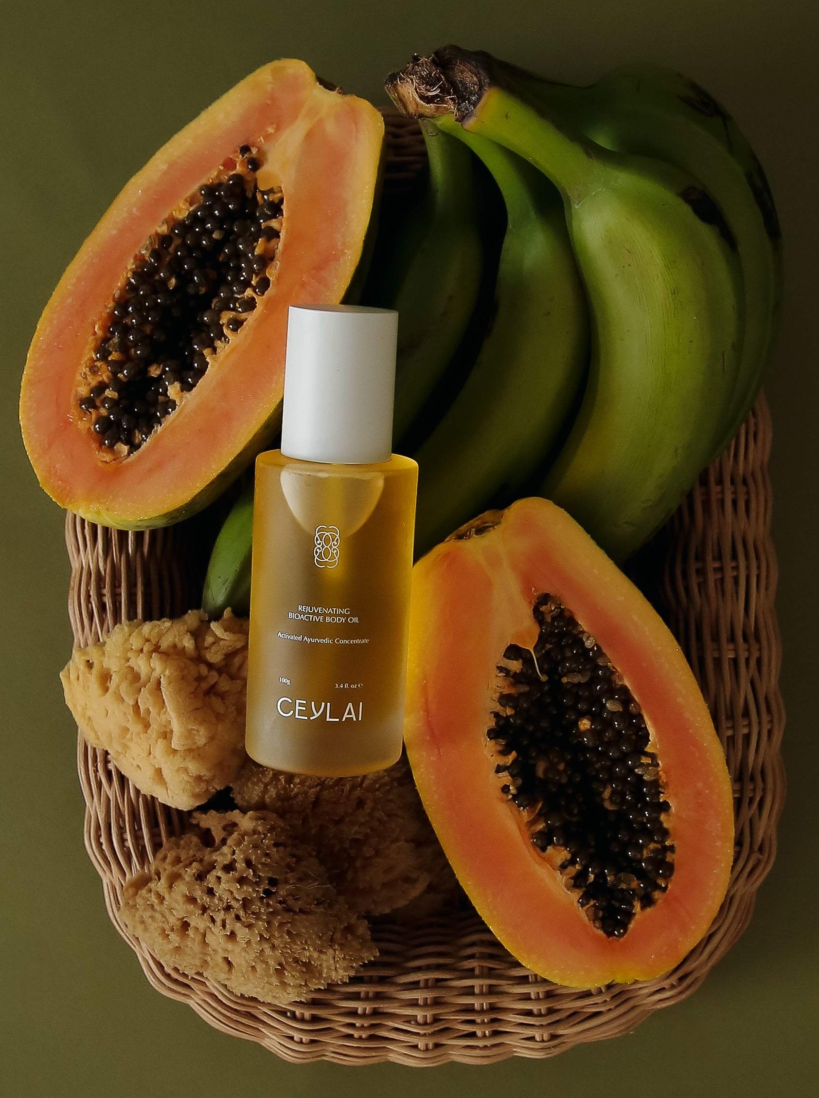 Ceylai body oil bottle with papaya and banana in a basket on a dark background
