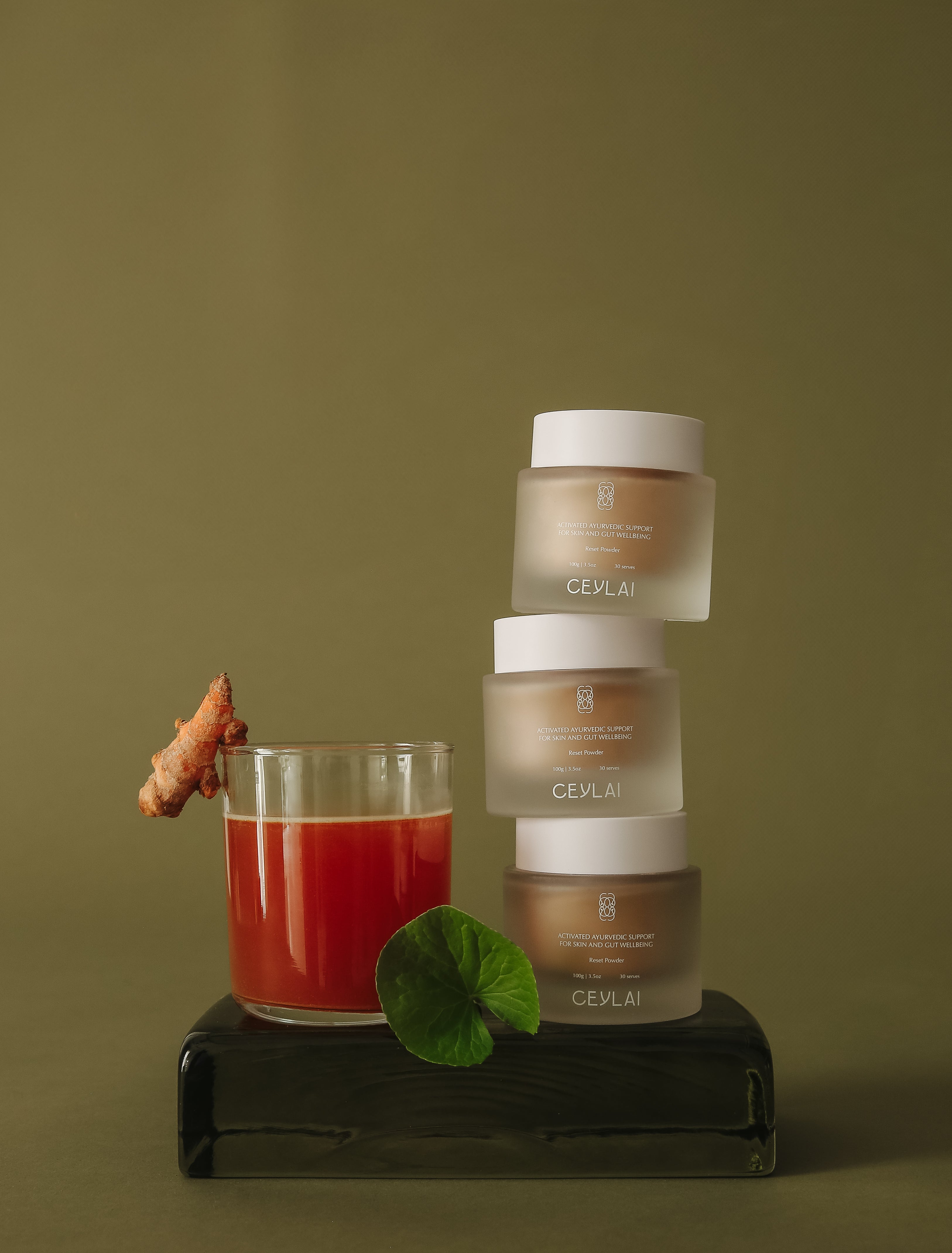 Stack of Ceylai Reset Powder jars with a glass of reset powder and a leaf and tumeric on a green background.